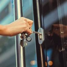 Hands unlocking a secure lock on a glass door with keys.