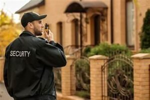 A security guard looking at a house to his right while talking on the radio.