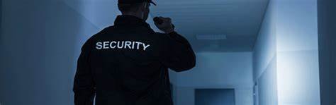 A security guard using his flashlight to see the door in front of him.